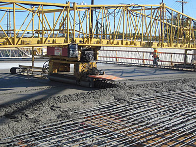 Maquina de colado de concreto (Bidwell) pone el nuevo concreto sobre la superficie del puente.