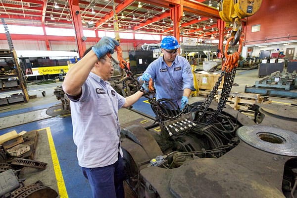 Fuyuong Chung, a la derecha, y Josue Moir se preparan para levantar el carro que sostiene las llantas de los trenes para ser instaladas en un vagón del tren ligero.